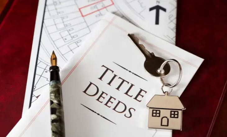 Key and House Keychain Laying on Top of Title Deeds Document